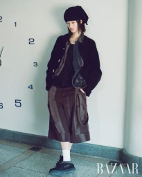 Model in black cap, dark jacket, and patterned trousers standing against a wall with clock numbers for Harper's Bazaar Korea
