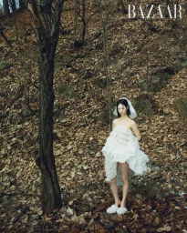 Model Chloe Oh in a white textured dress and veil standing on a leaf-covered woodland slope for Harper's Bazaar Korea.