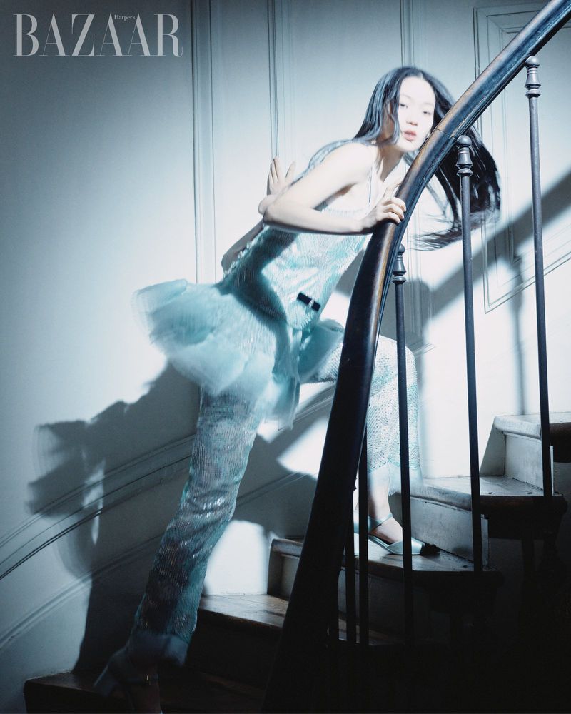 Fashion editorial shot of a young Asian woman on a staircase wearing a light blue shimmering two-piece outfit, and shiny silver heels.