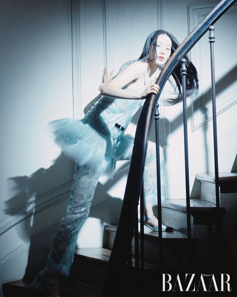 Elegant Asian woman descends staircase in shimmering blue gown and matching trousers, creating a sophisticated and stylish fashion moment.