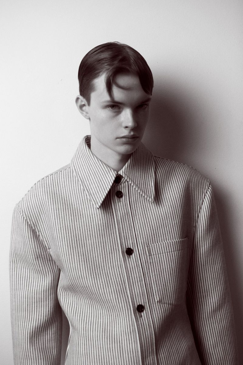 Monochrome portrait of a young man in a striped jacket against a neutral background, showcasing a blend of fashion and portraiture.