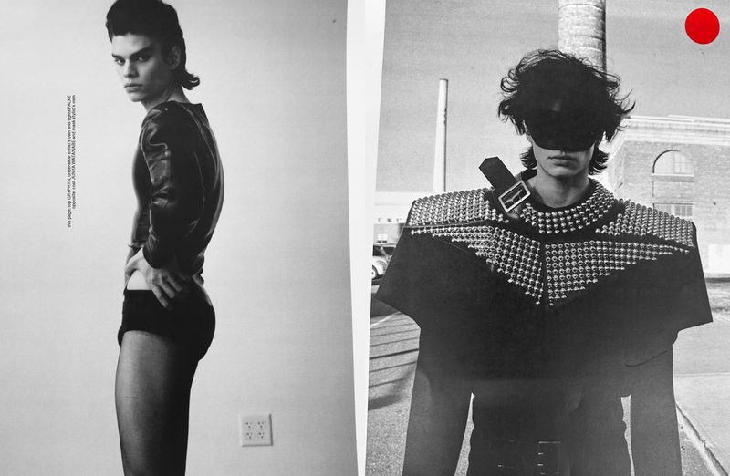 Black and white studio shot of male fashion model in dramatic couture with industrial backdrop and red dot graphic element, editorial style.