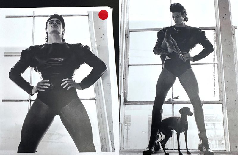 Black-and-white fashion image of a male model in a black bodysuit posing by a window with a dog at his feet. High-contrast lighting.