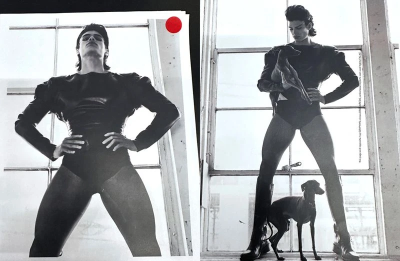 Black-and-white fashion image of a male model in a black bodysuit posing by a window with a dog at his feet. High-contrast lighting.
