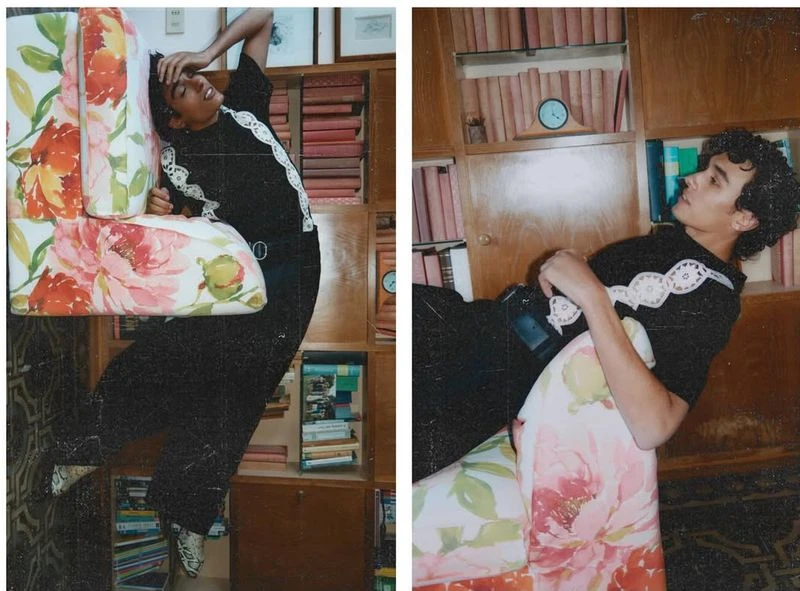 Young adult lies on floral-patterned couch in a room with wood-paneled walls and a bookshelf filled with books in a brightly lit setting.
