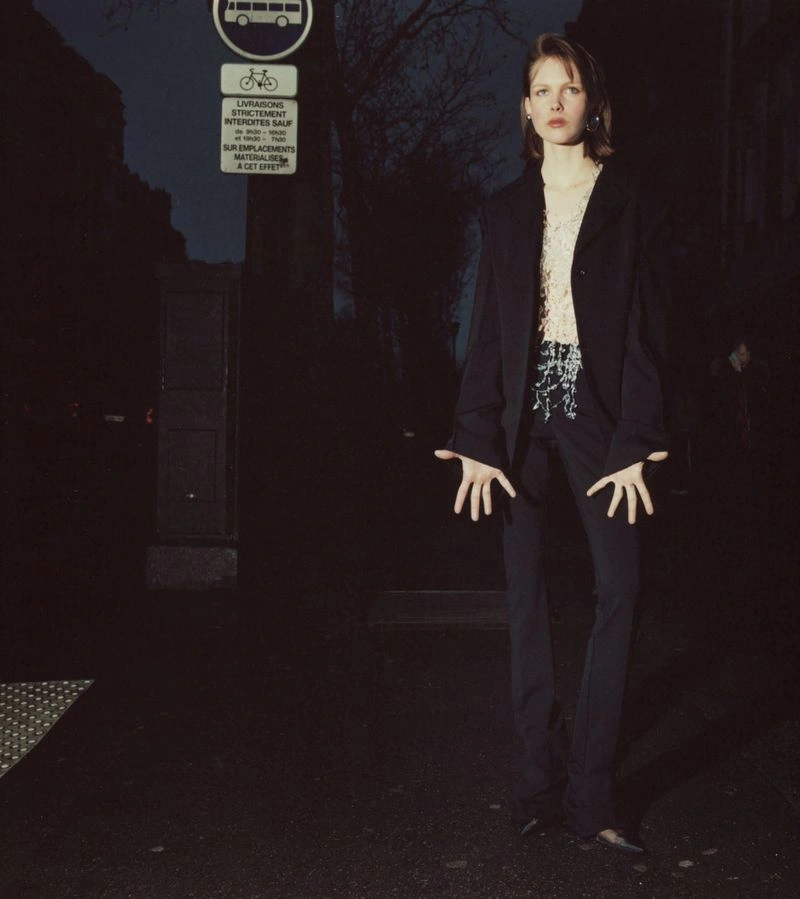 Model standing on a dark city street at night wearing a black blazer and trousers with hands held out