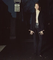 Model standing on a dark city street at night wearing a black blazer and trousers with hands held out