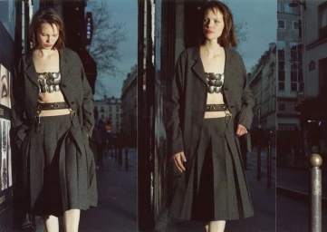 Model wearing a grey blazer, pleated skirt, and metal disc top standing on a city street at dusk for Muse Magazine.