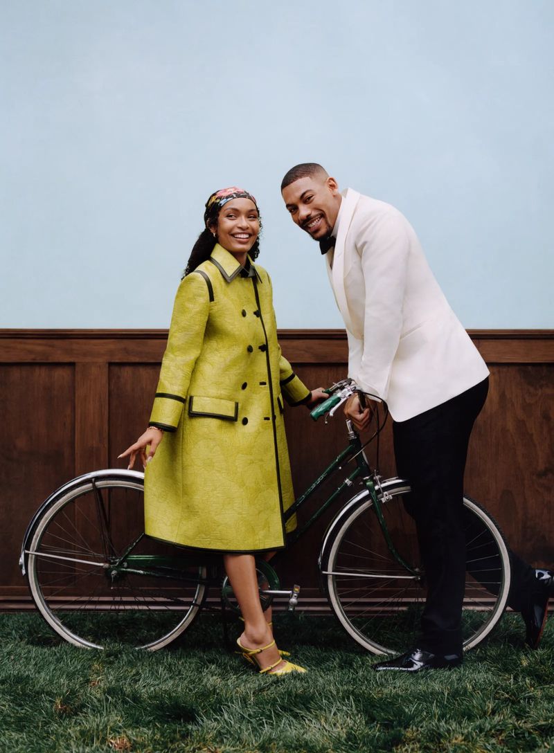 A stylish couple poses with a vintage bicycle against a pale blue backdrop, showcasing formal wear and a touch of retro flair.