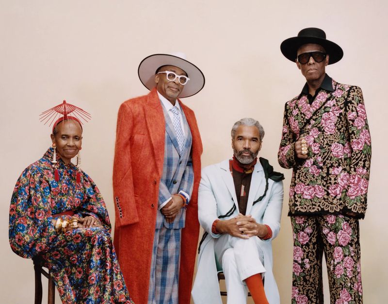 Group portrait of four stylishly dressed people in a studio setting, showcasing diverse fashion styles and posing against a neutral backdrop.
