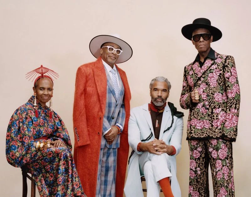 Group portrait of four stylishly dressed people in a studio setting, showcasing diverse fashion styles and posing against a neutral backdrop.