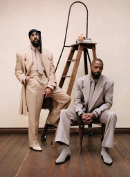 Two Black men in tailored beige suits posing near a wooden ladder in an editorial portrait for American Vogue.