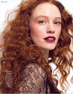 Close-up beauty portrait of a woman with curly red hair and dark burgundy lipstick wearing black lace against a white background