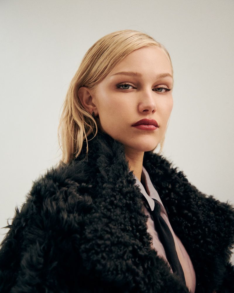 Portrait of Grace VanderWaal wearing a black textured coat and tie against a plain light background