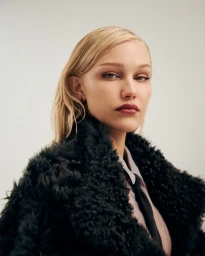 Portrait of Grace VanderWaal wearing a black textured coat and tie against a plain light background