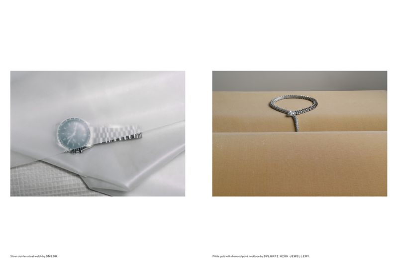 Elegant jewelry editorial featuring a silver Omega watch on white fabric and a Bulgari necklace on a tan platform, shot indoors.