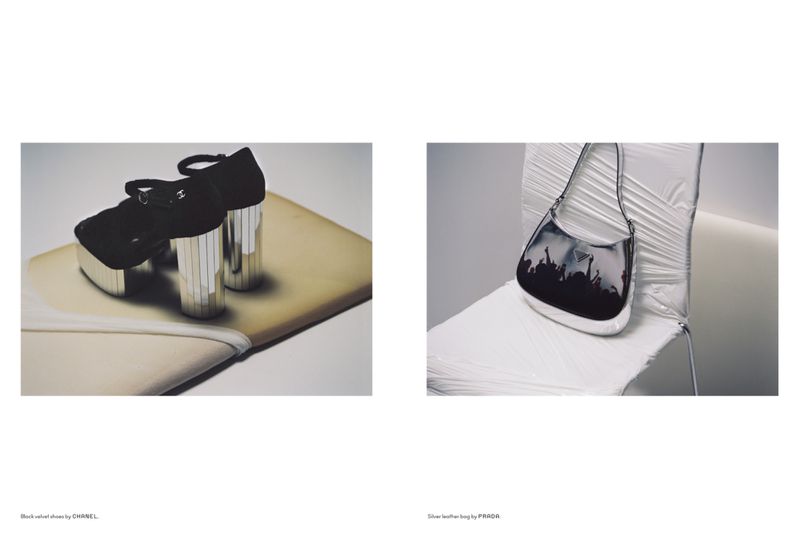 Fashion editorial showcasing a black platform heel shoe by Chanel and a silver leather bag by Prada, displayed on a draped surface in a studio.