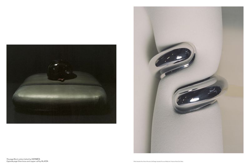 Still life shot of a black object on a reflective surface, and a silver cuff bracelet on a white sculptural stand, studio lighting.
