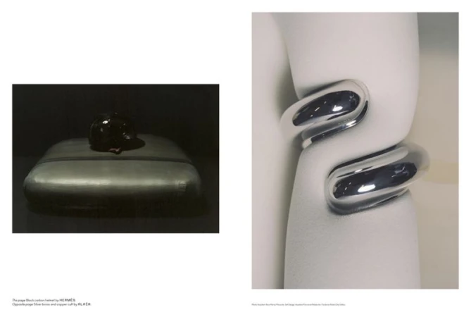 Still life shot of a black object on a reflective surface, and a silver cuff bracelet on a white sculptural stand, studio lighting.