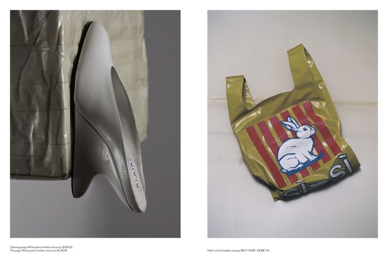 Studio shot of a white sculptural shoe and a plastic shopping bag with a white rabbit print against a white and grey backdrop.