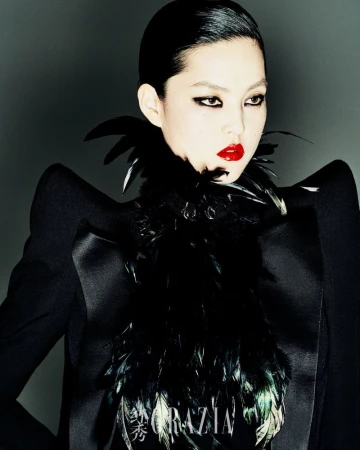 A striking portrait of an Asian woman with red lips, dramatic eye makeup, and feathered collar, wearing a dark jacket against a grey background.