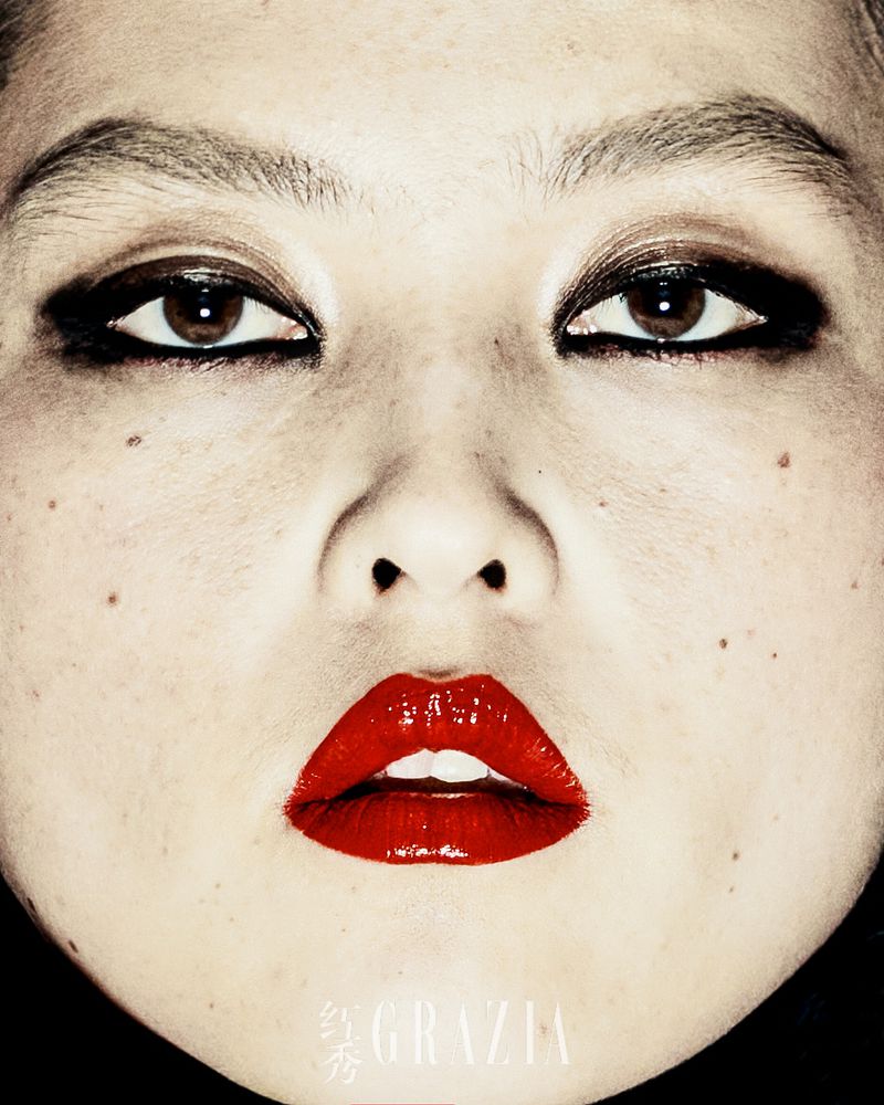 Close-up portrait of a young Asian woman with heavy dark eye makeup and glossy red lipstick, with GRAZIA magazine logo at the bottom.