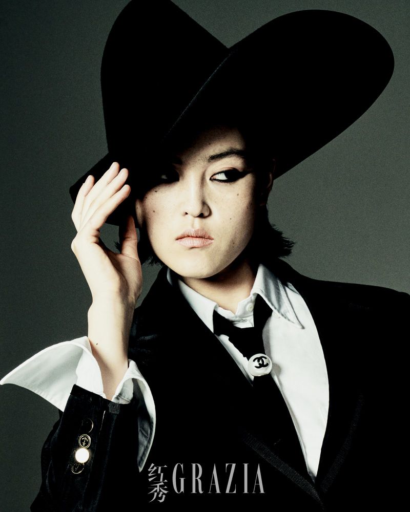 Model Xue Gu wearing a black wide-brimmed hat, blazer, white shirt, and tie for Grazia China by Rambo Ding.