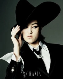 Model Xue Gu wearing a black wide-brimmed hat, blazer, white shirt, and tie for Grazia China by Rambo Ding.
