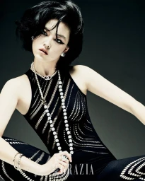 Model Xue Gu in a black patterned top with layered pearl necklaces and heavy winged eyeliner against a grey seamless background