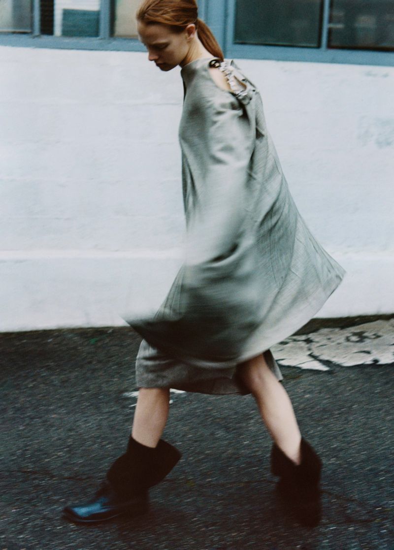 Fashionable woman walking on a wet street wearing a stylish grey dress and black boots, showcasing a contemporary and elegant look.