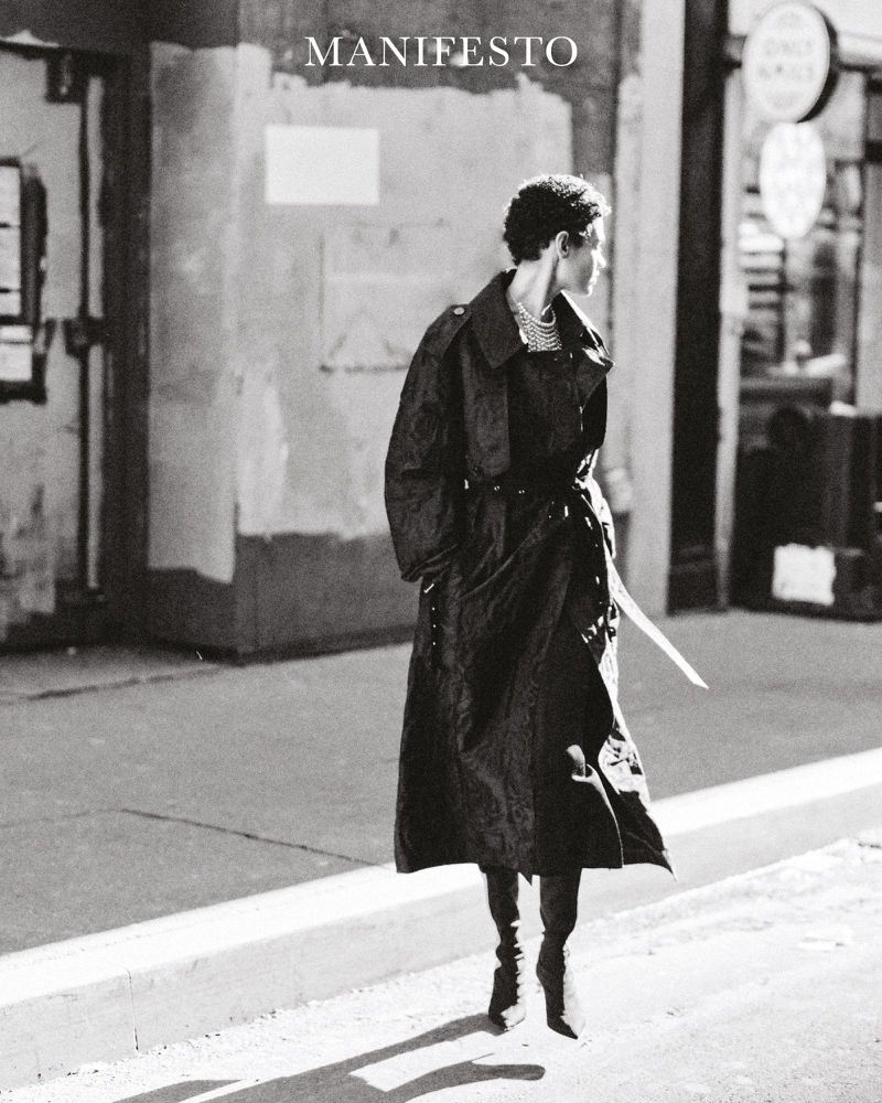 Model Kerolyn Soares in a dark trench coat walking on a city street for Manifesto Magazine