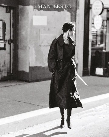 Model Kerolyn Soares in a dark trench coat walking on a city street for Manifesto Magazine