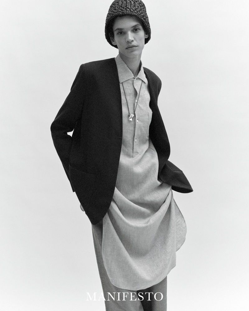 Model Kerolyn Soares wearing a black blazer over a long light tunic and a textured knit cap against a plain white background.