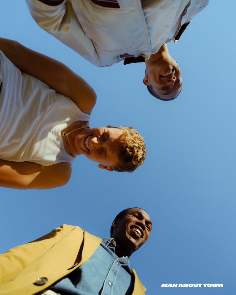 Low-angle shot of three smiling young adult men in casual attire against a clear blue sky, suggesting a lighthearted, youthful vibe.