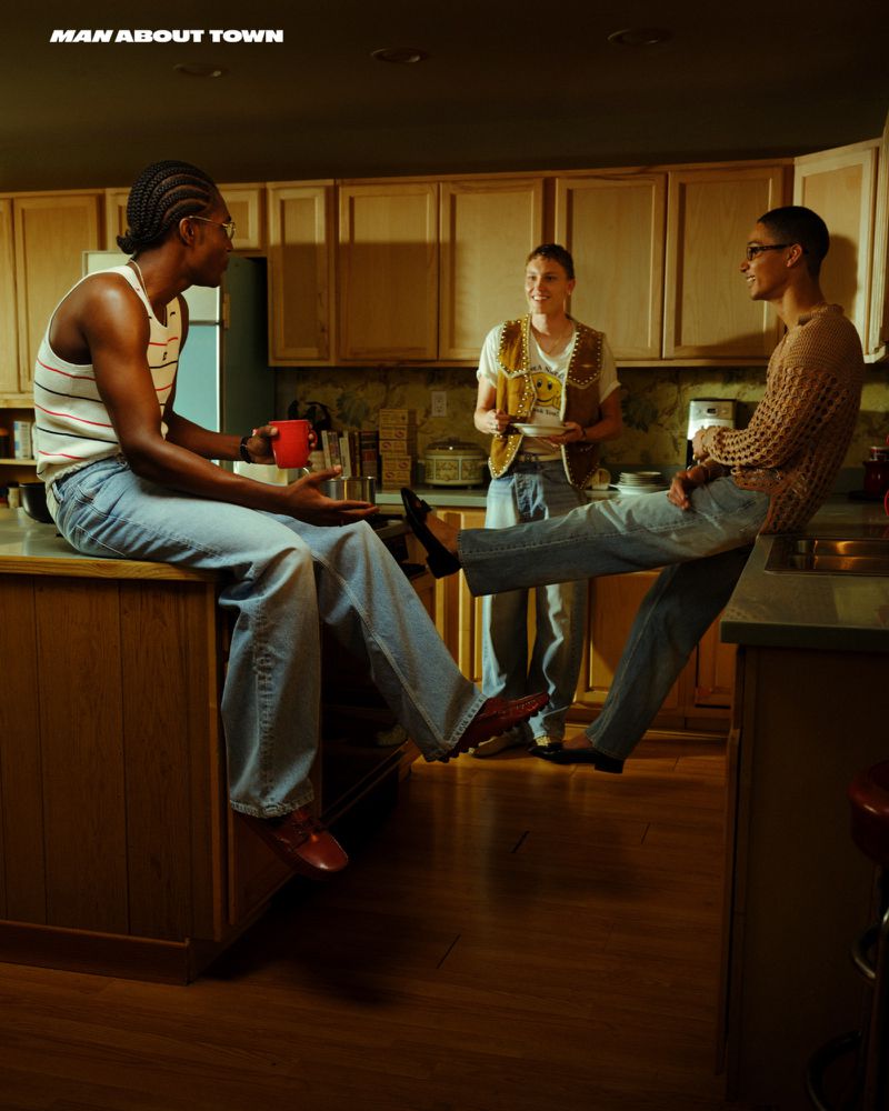 Three people in a kitchen, one man with a red cup sitting on the counter, another standing, and another sitting on the counter.