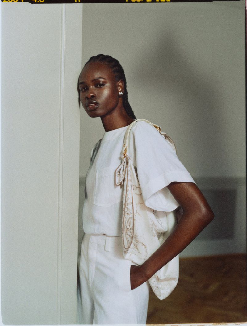 Model Bakhita Lual in white attire leaning against a wall for Harper's Bazaar UK photographed by Cornelius Kaess