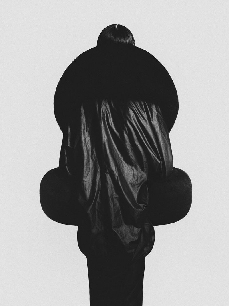 Monochrome studio shot of an unidentifiable person with spherical padding and dark fabric against a bright neutral backdrop.