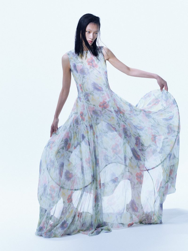 Fashion shoot featuring an Asian model in a flowing floral dress against a white backdrop, full shot, demonstrating style and elegance.