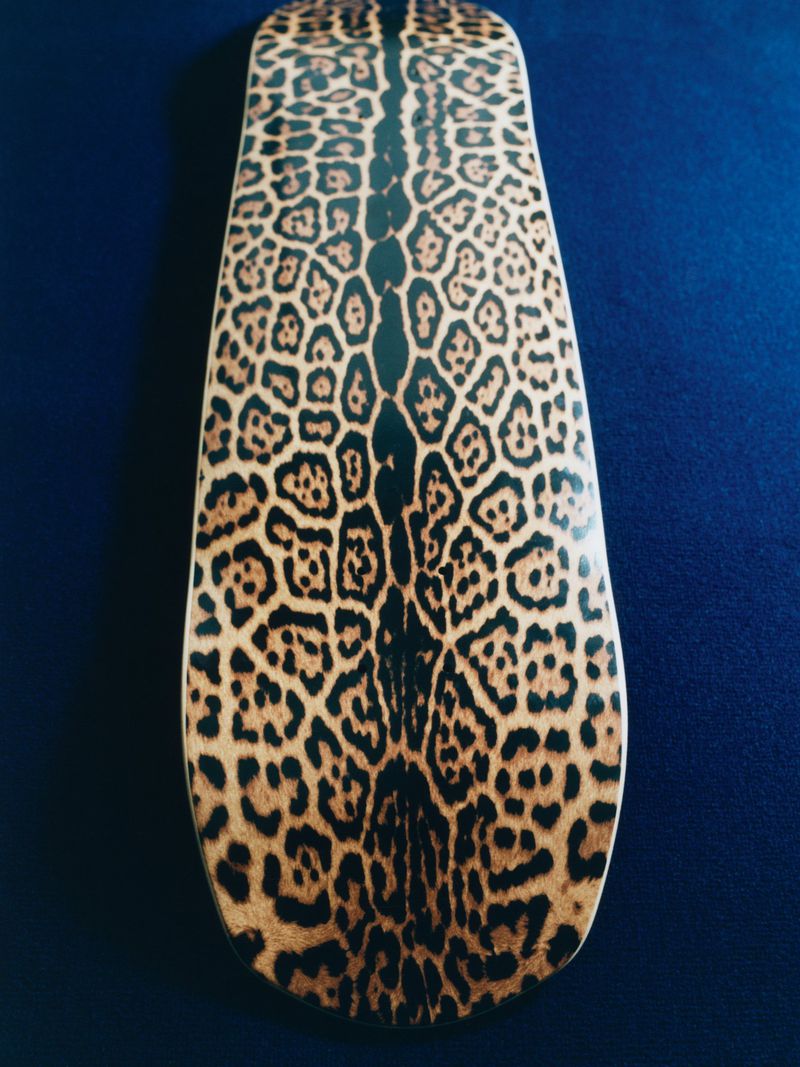 Skateboard deck featuring a spotted animal print on a blue background. The graphic is positioned vertically in the frame.