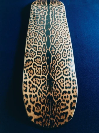 Skateboard deck featuring a spotted animal print on a blue background. The graphic is positioned vertically in the frame.
