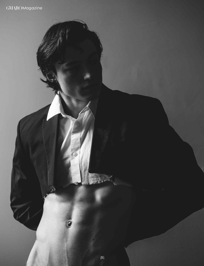 Monochrome portrait of a male model with an open dress shirt and blazer, showing off toned abdominal muscles against a grey background.