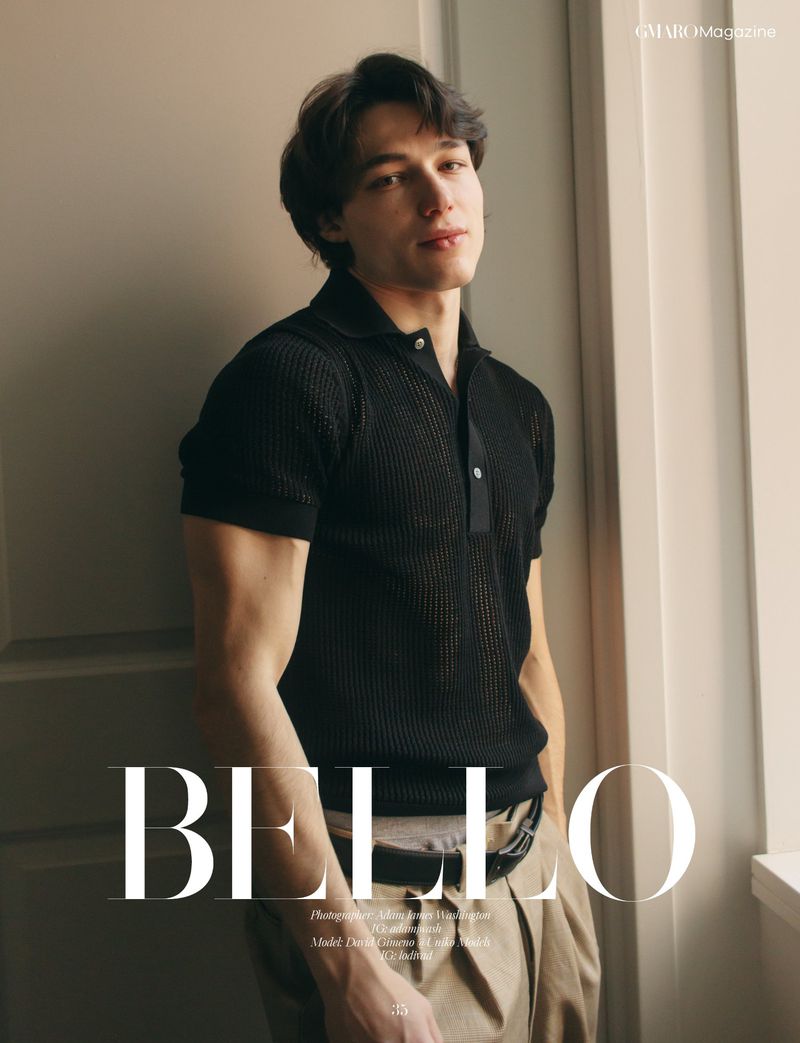 Portrait of a young man in a black collared shirt and tan pants, leaning against a wall with a window, studio lit, fashion editorial.