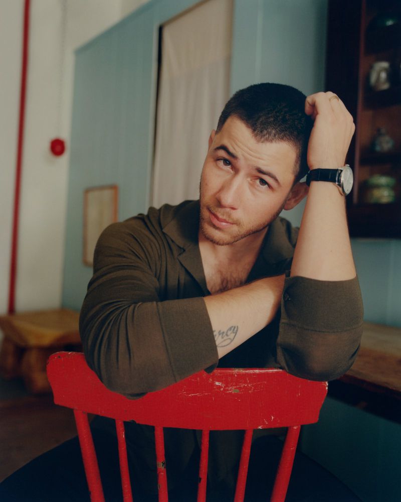 Portrait of adult male with short hair in a green shirt, sitting on a red chair indoors and resting his arm on the chair's back.