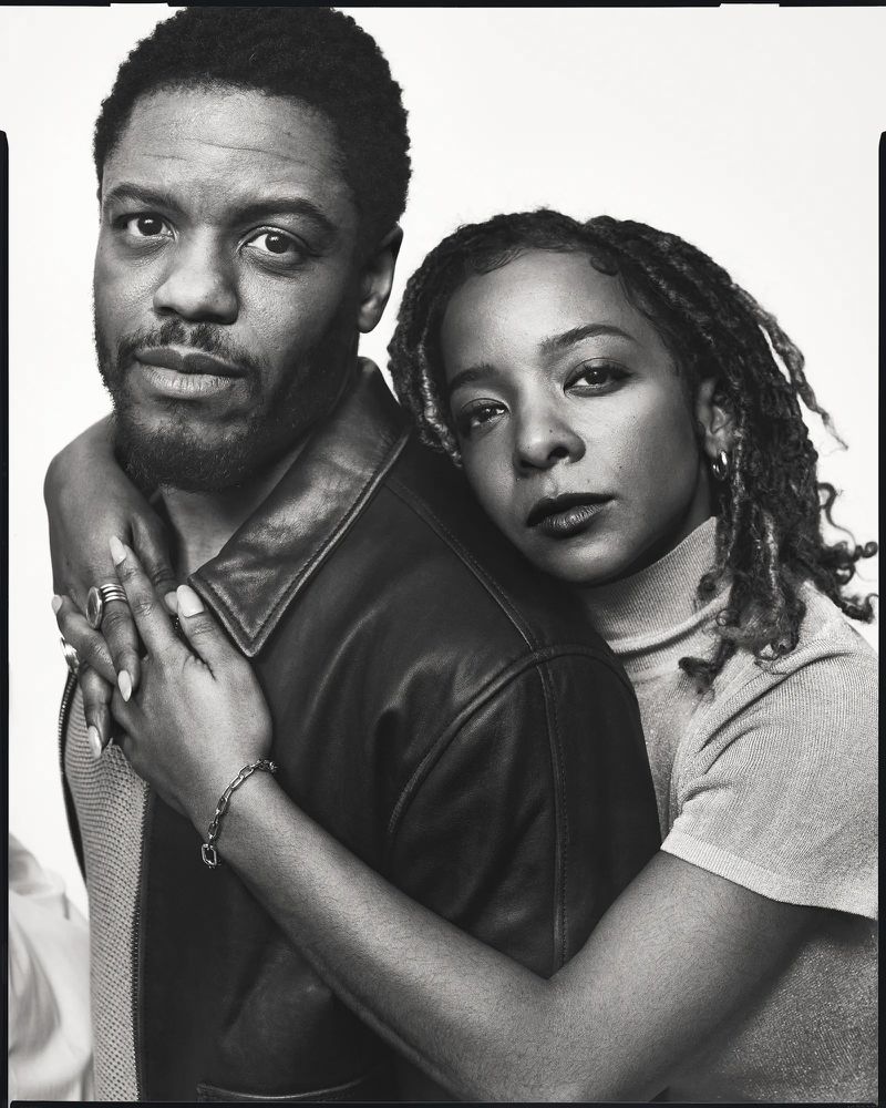 Monochrome portrait of a Black man and Black woman embracing in a studio, showcasing textured hair and clothing details in sharp focus.