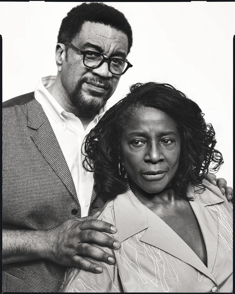 Black and white portrait of two adults posing against a plain background for American Vogue.