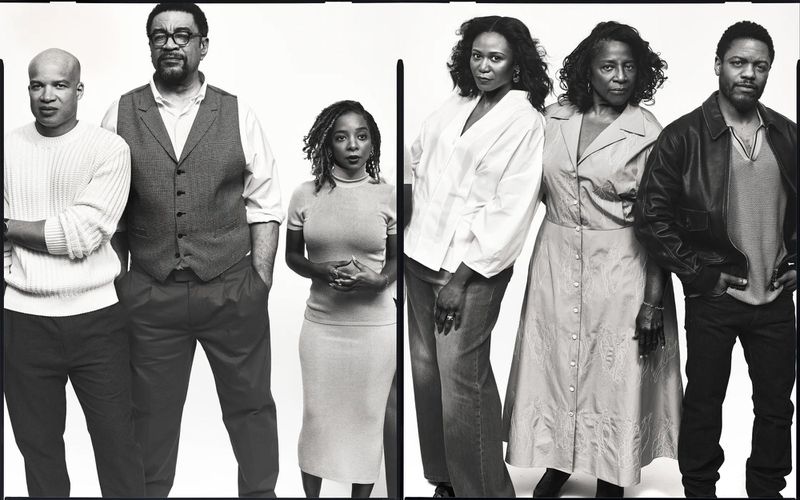 Black and white studio portrait of six Black adults standing shoulder to shoulder in casual wear against a seamless white backdrop.