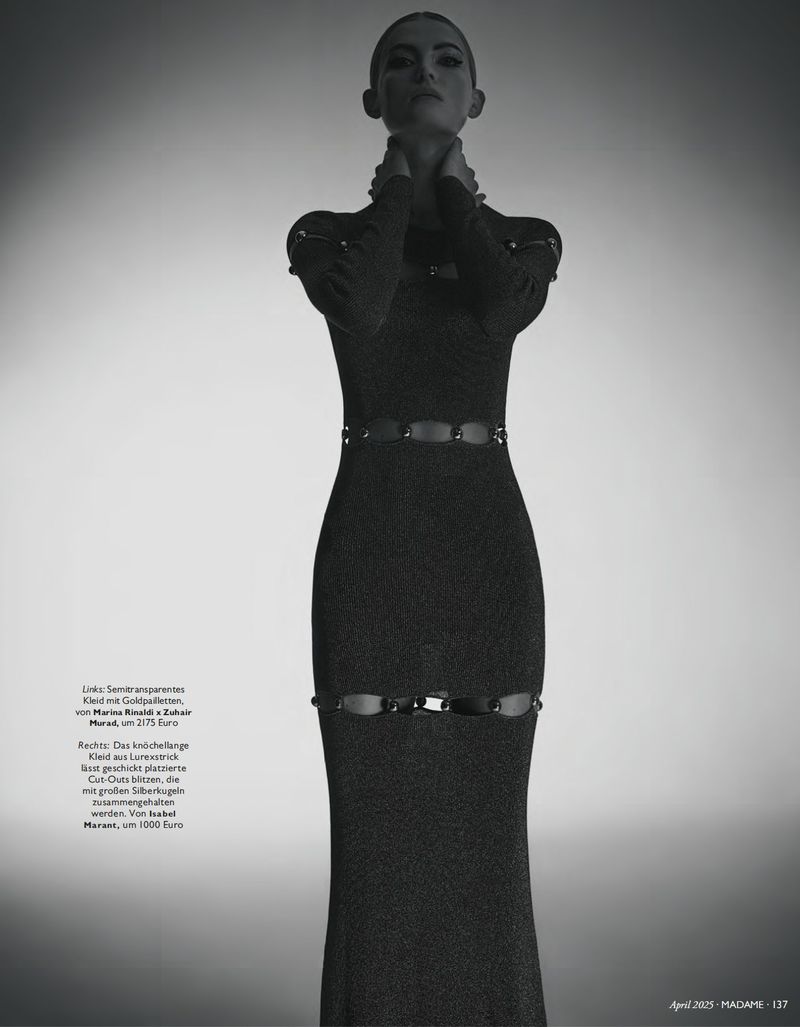 Monochrome fashion shot of a woman in a long-sleeved gown with cut-out details, posing against a gradient background in a studio.