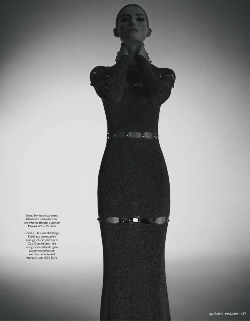 Monochrome fashion shot of a woman in a long-sleeved gown with cut-out details, posing against a gradient background in a studio.