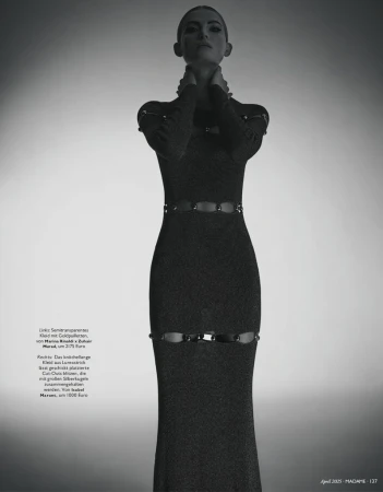 Monochrome fashion shot of a woman in a long-sleeved gown with cut-out details, posing against a gradient background in a studio.
