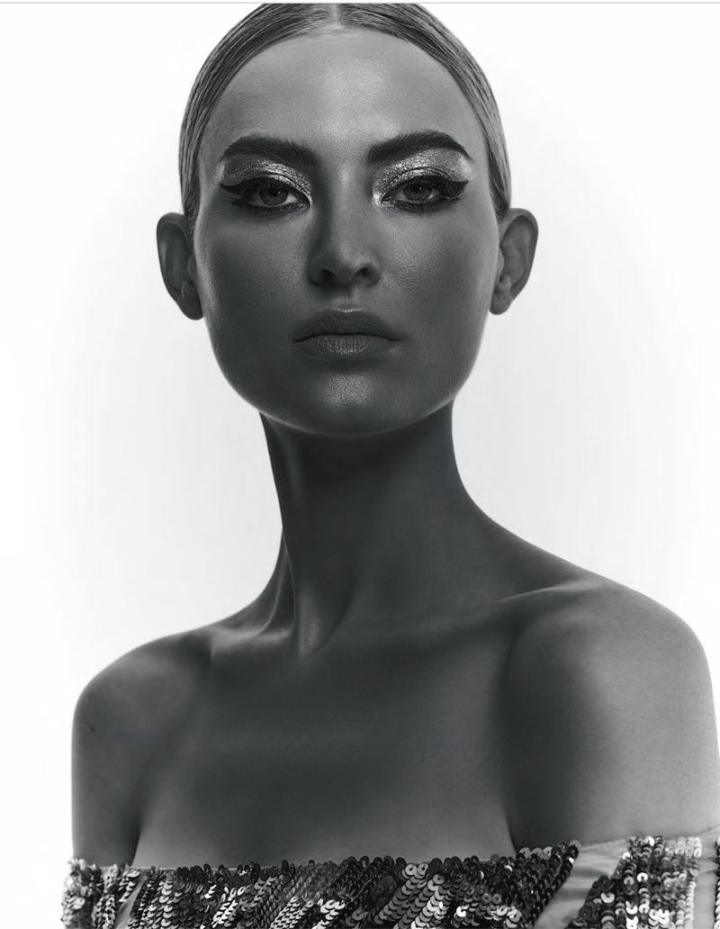 Striking black and white close-up of a woman with dramatic makeup and sequin top against a stark white background, capturing her intense gaze.
